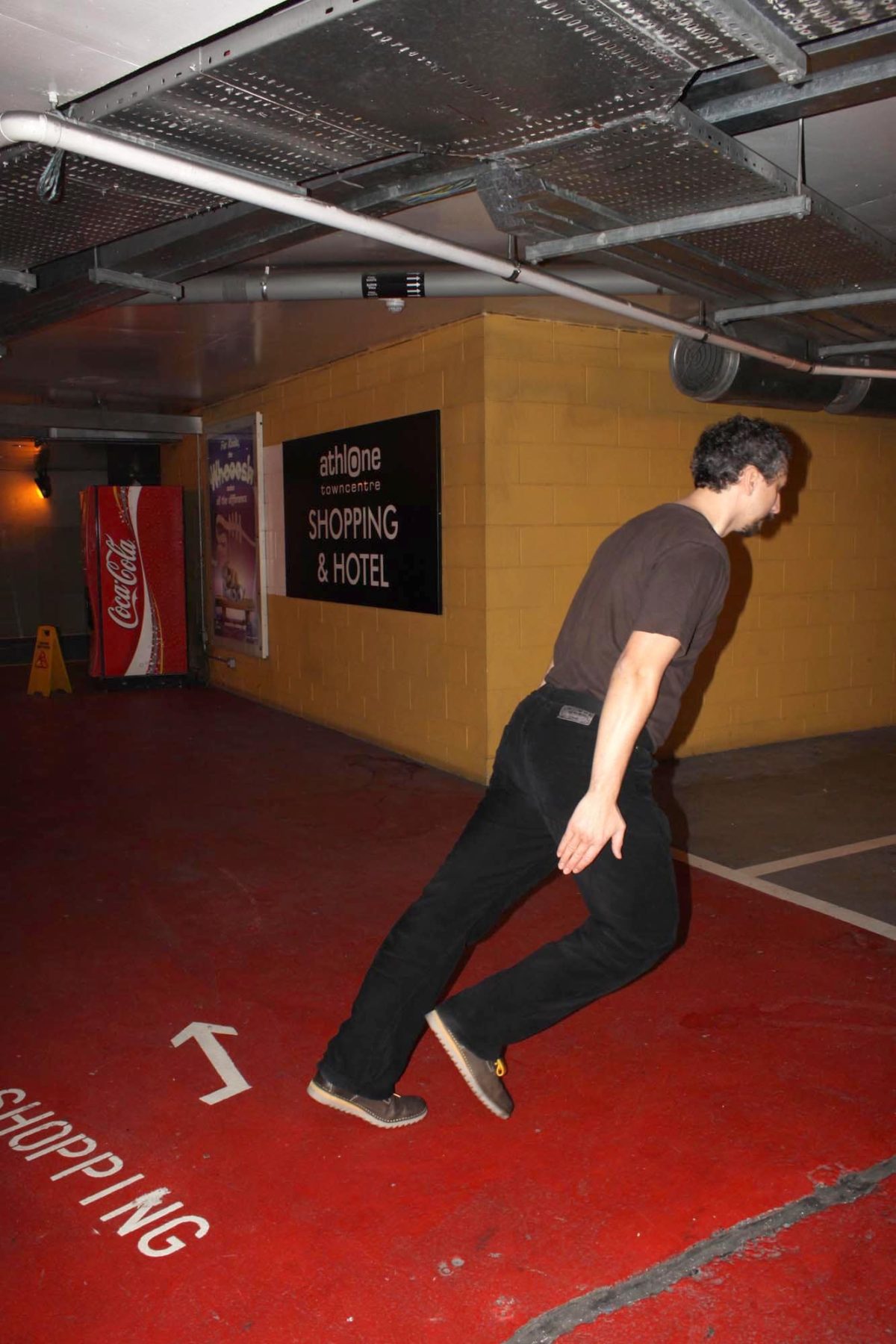 Artist making a diagonal with his body in a subteran parking lot of a shopping centre.